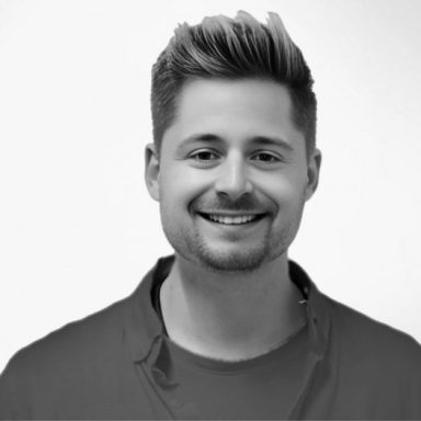 Thimo Gimmerthal Lächelnder Mann mit kurzen, blonden Haaren und schwarzer Jacke vor einem hellen Hintergrund.